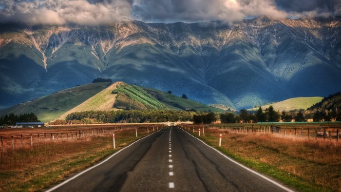 Road leading to mountains under cloudy sky