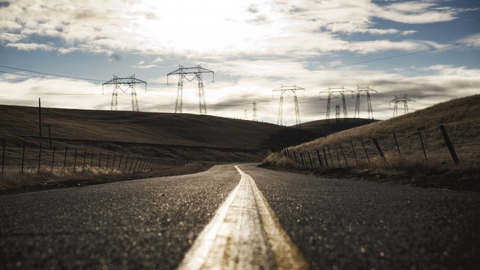 Road leading to power lines on rolling hills