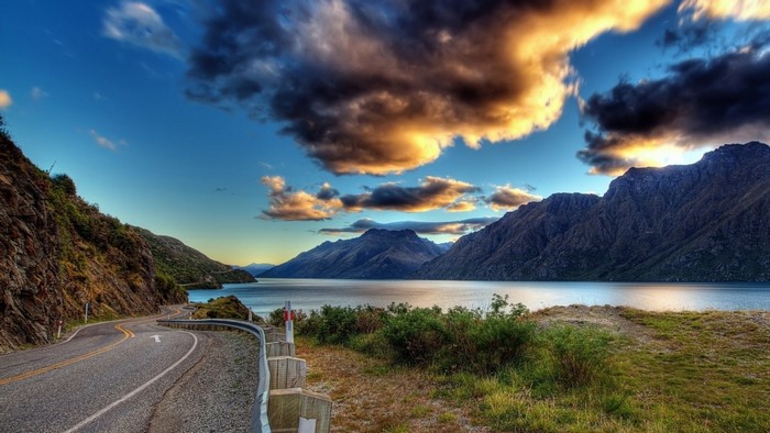 Winding road along a lake with mountains at sunset