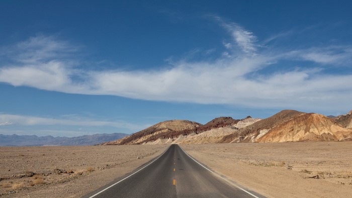 Desert road leading to colorful mountains under a blue sky