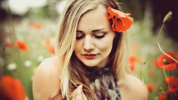 Woman with red poppy in her hair in a field of poppies