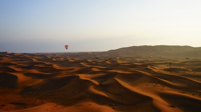 Hot air balloon over desert dunes at dawn