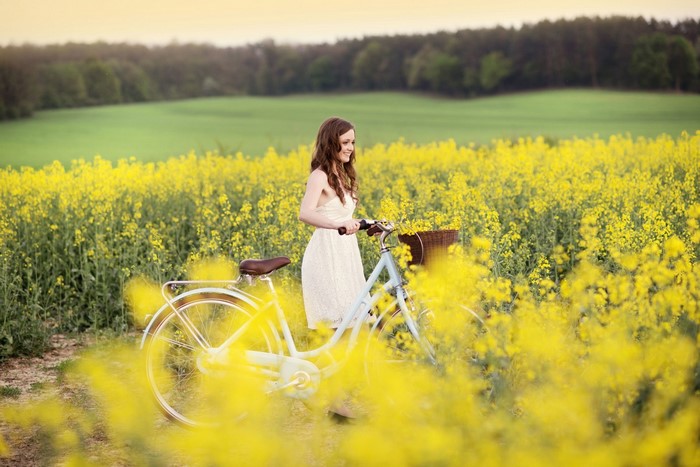 Woman with bicycle in a field of yellow flowers