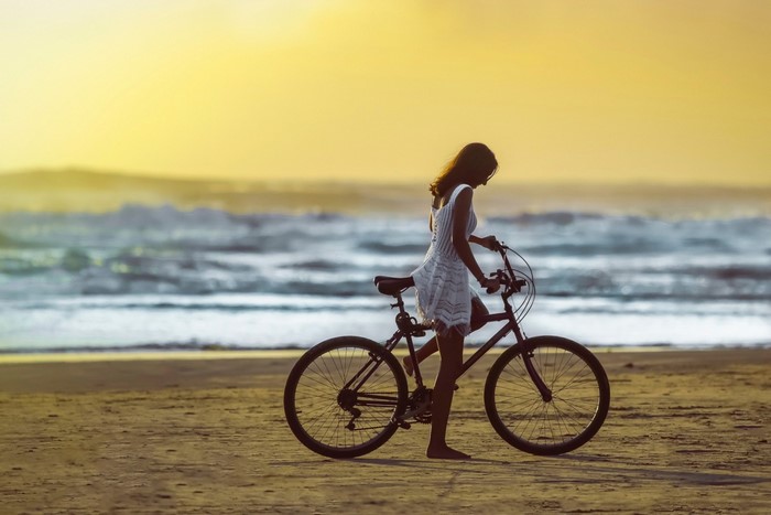 Woman with bicycle on beach at sunset