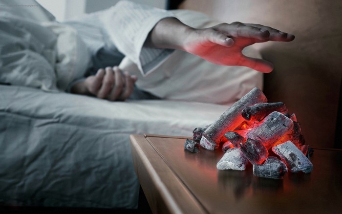 Person warming hand over glowing coals in bed