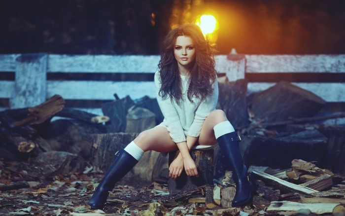 Woman in sweater and boots sitting outdoors