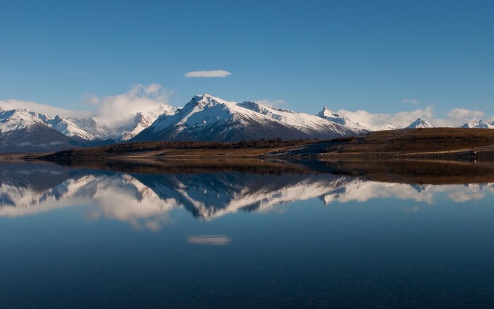 Snow-capped mountains reflected in a calm lake under a blue sky