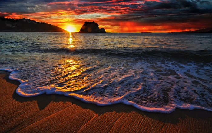 Sunset over the ocean with waves crashing on the beach