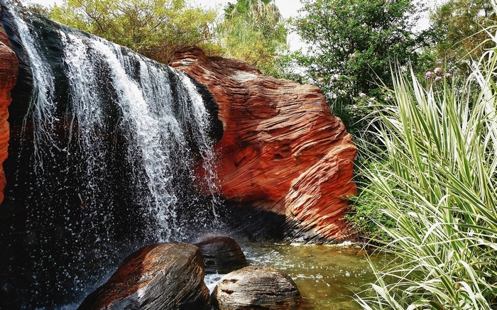 Waterfall cascading over red rocks with lush greenery