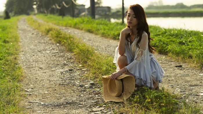Woman in a light blue dress with a hat on a dirt road