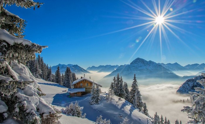 Snowy mountain landscape with a cabin and sun rays