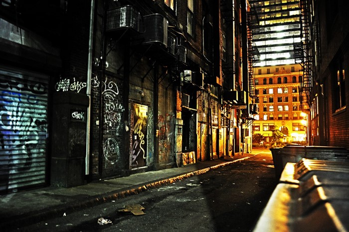 Graffiti-covered alleyway at night with city buildings