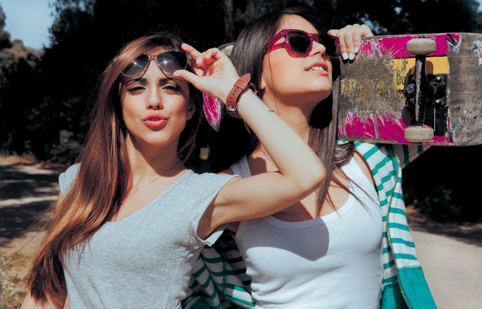 Two young women with sunglasses and a skateboard