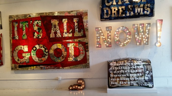 Art display with "It's All Good" and "Now!" signs