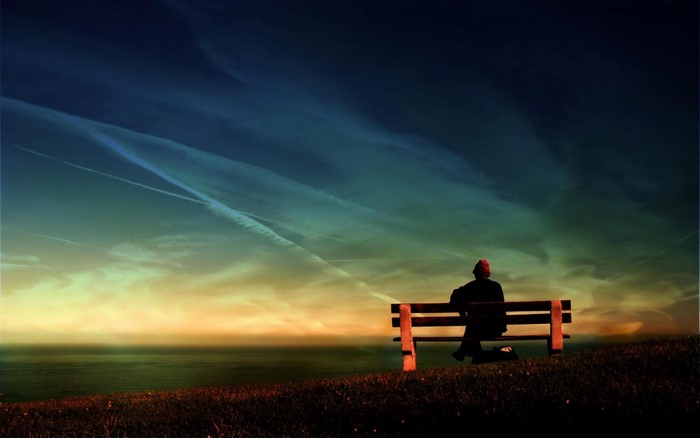 Person sitting on a bench overlooking the ocean at sunset