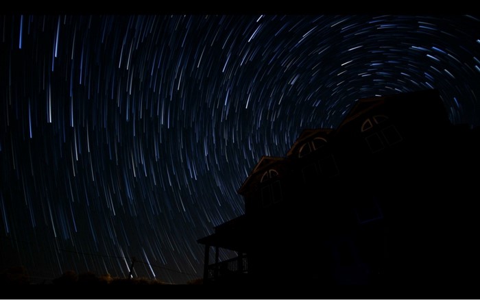 Star trails over a silhouetted house at night