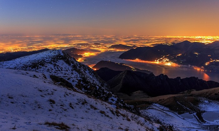 Snowy mountain peak overlooking a misty city at night