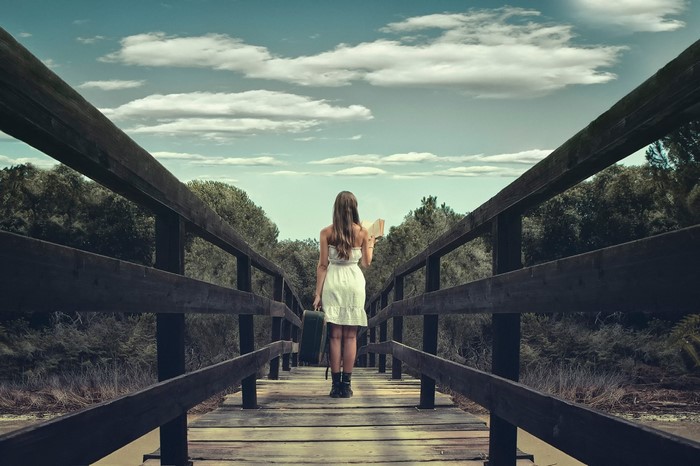 Woman with suitcase and book on a wooden bridge