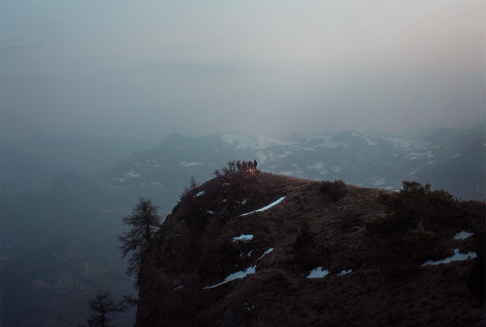 People gathered around a campfire on a mountain ridge at dawn
