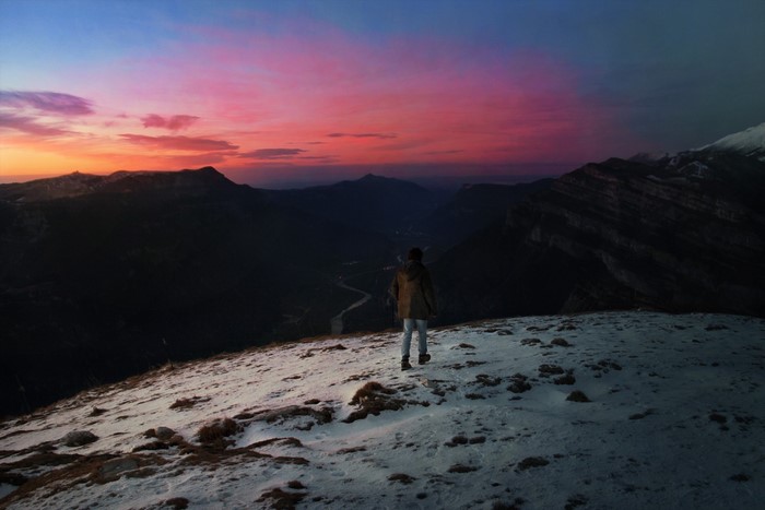 Person on snowy mountain ridge at sunset