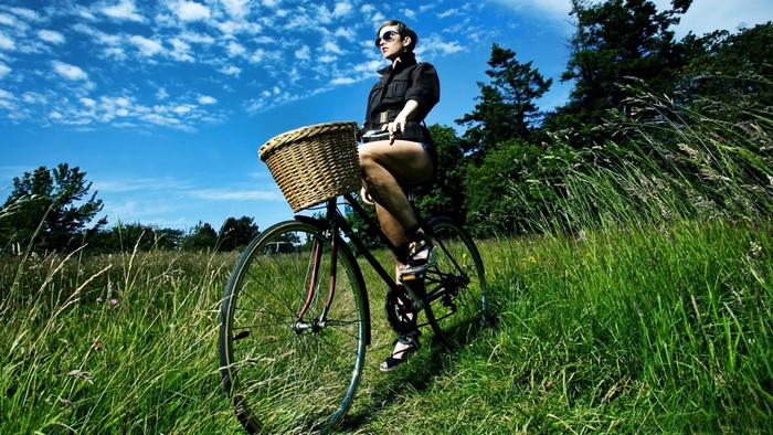 Woman on a bicycle with a basket in a grassy field