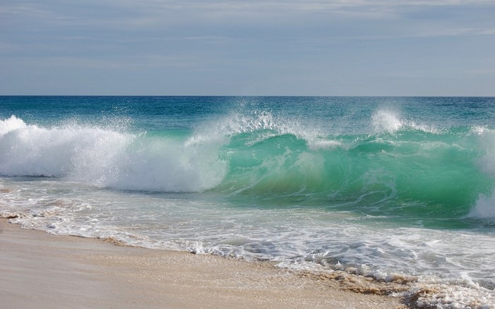 Turquoise wave crashing on a sandy beach