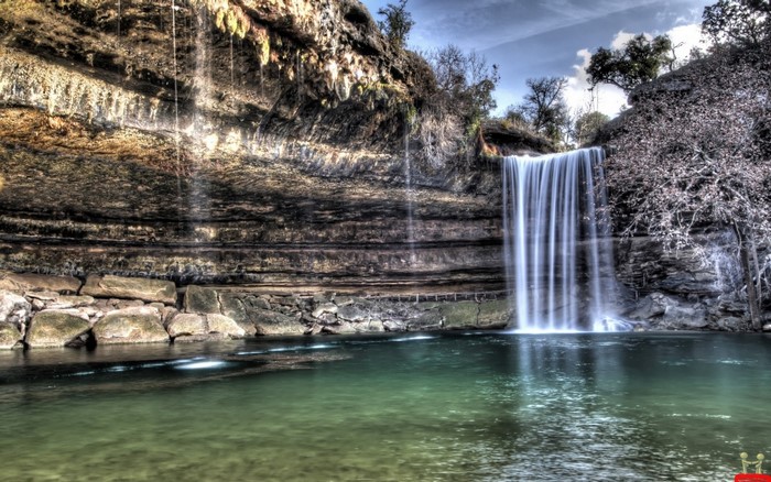 Waterfall cascading into a clear pool surrounded by rocks and trees