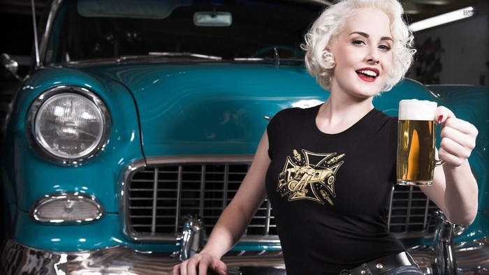 Woman holding a beer in front of a vintage car