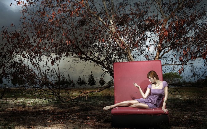 Woman in purple dress sitting on red couch under tree