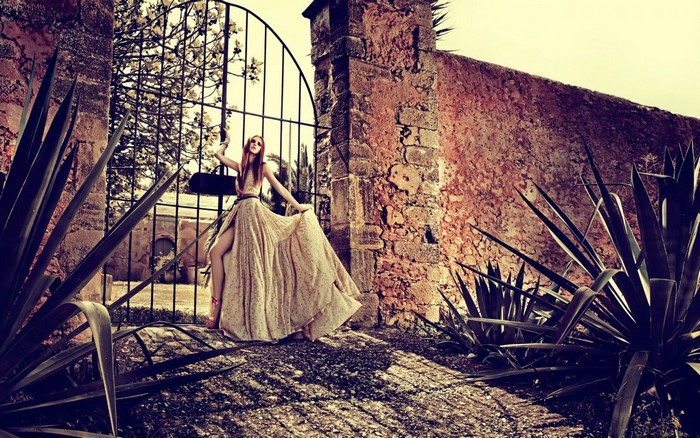 Woman in flowing dress by ancient stone wall and gate