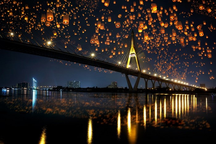Sky lanterns float over a bridge at night
