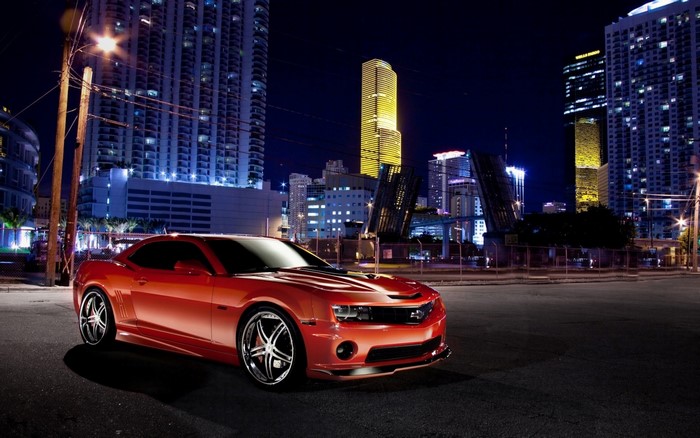 Red Chevrolet Camaro parked in a city at night