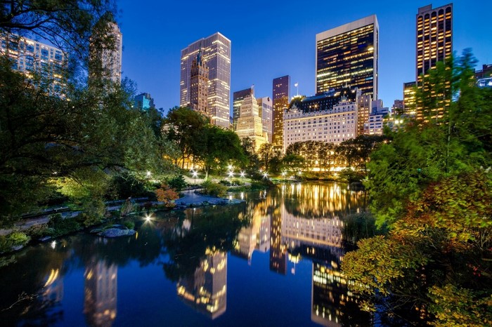 Central Park pond reflecting New York City skyline at dusk