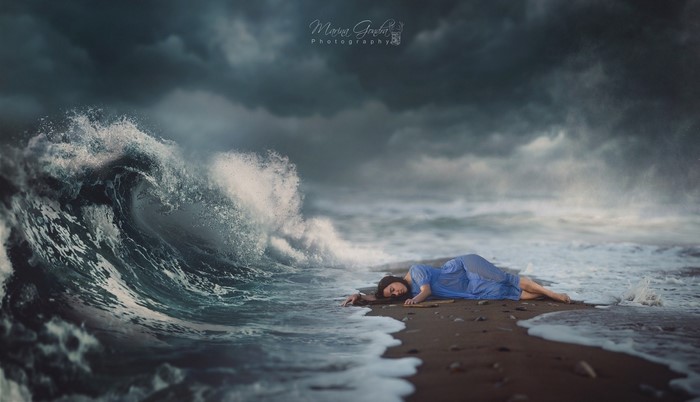 Woman in blue dress lying on beach during storm