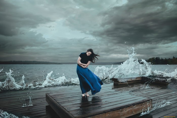 Woman in blue skirt on a pier with waves crashing