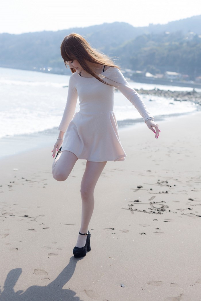Asian woman in dress on beach stretching leg