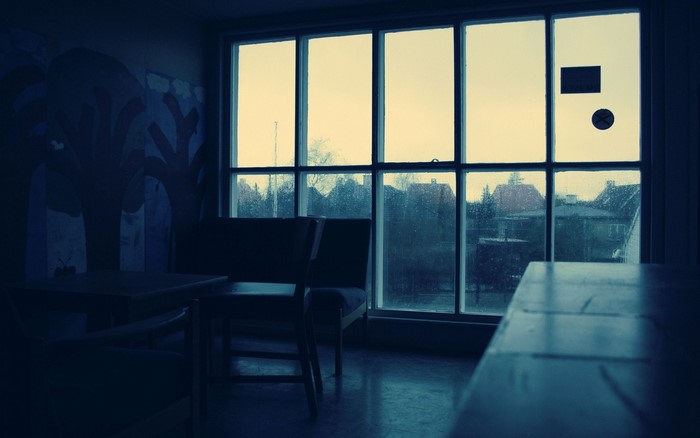 Interior room with large window overlooking houses in the rain