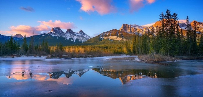 Three Sisters mountains reflected in a frozen lake at sunrise