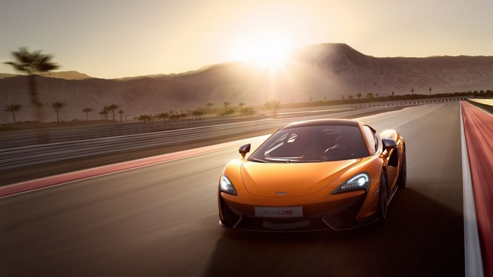 Orange McLaren 570S sports car on a race track at sunset