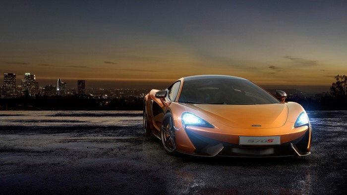 Orange McLaren 570S sports car at dusk with city skyline