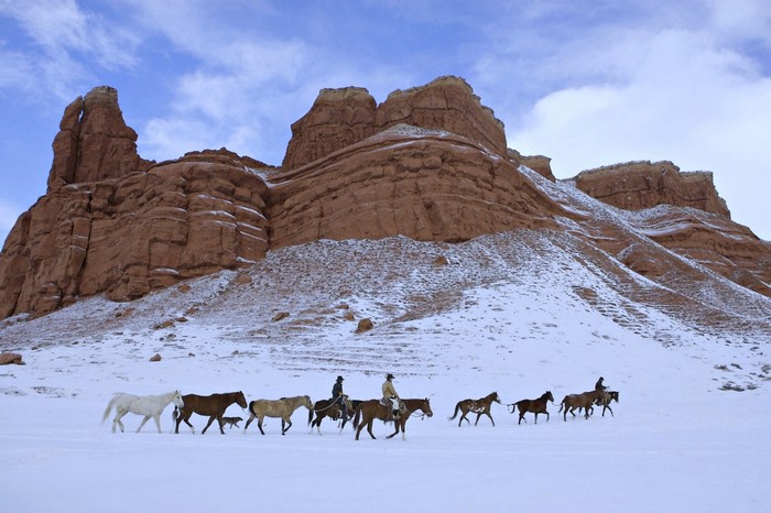 Cowboys riding horses through a snowy landscape with rock formations