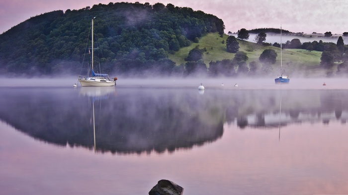 Sailboats on a foggy lake with hills