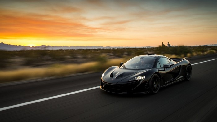 Black McLaren P1 driving on a desert road at sunset