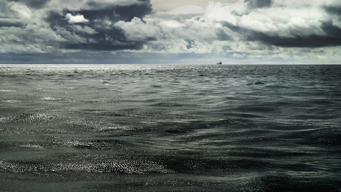 A lone ship on the horizon under stormy clouds