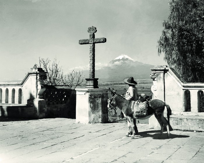Man with donkey and cross before volcano