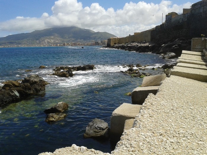 Rocky coastline with a fortified wall and a mountain in the distance