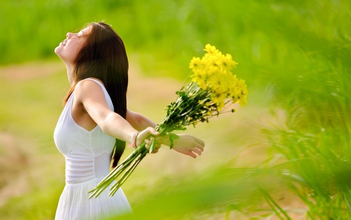 Woman in white dress holding yellow flowers in a field