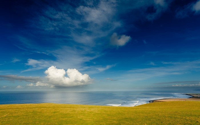 Grassy hill overlooking the ocean under a cloudy sky