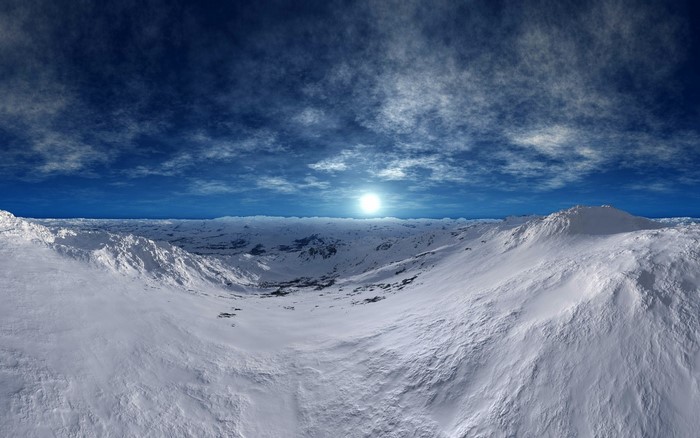 Snowy mountain landscape under a cloudy blue sky with a bright sun