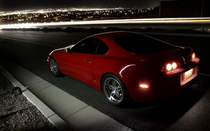 Red Toyota Supra parked at night overlooking city lights